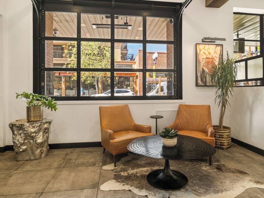 A modern interior with two leather chairs, a round table, and a large window offering a view of the street.