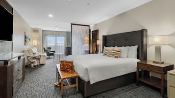 Habitación de hotel con una cama grande, un escritorio con silla, un sofá, un televisor y una ventana con cortinas.