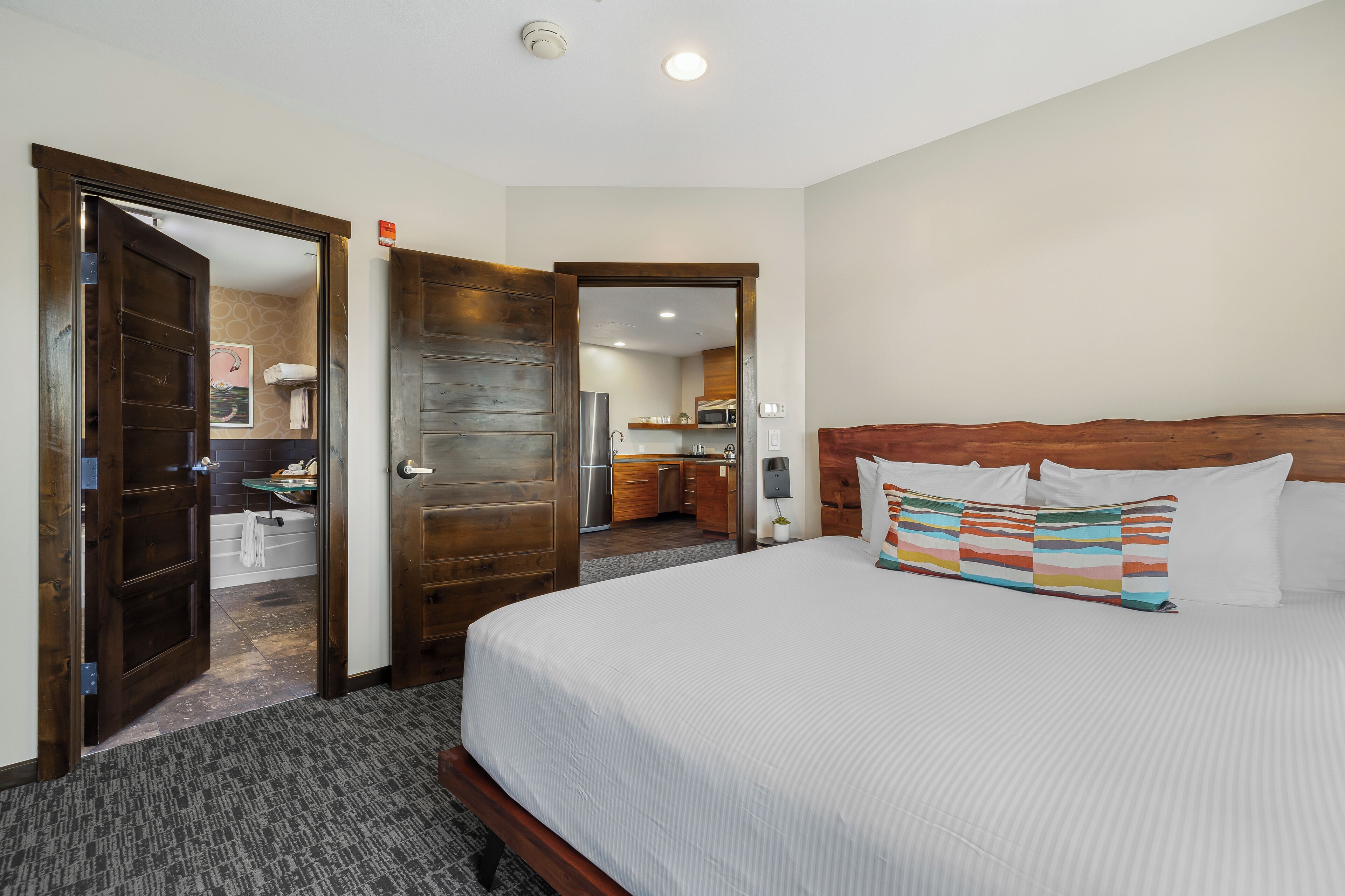 A hotel room with a large bed, wooden doors, a bathroom, and a kitchenette.