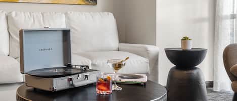 A modern living room with a white sofa, a round coffee table with a record player, a glass of whiskey, and a small potted plant.