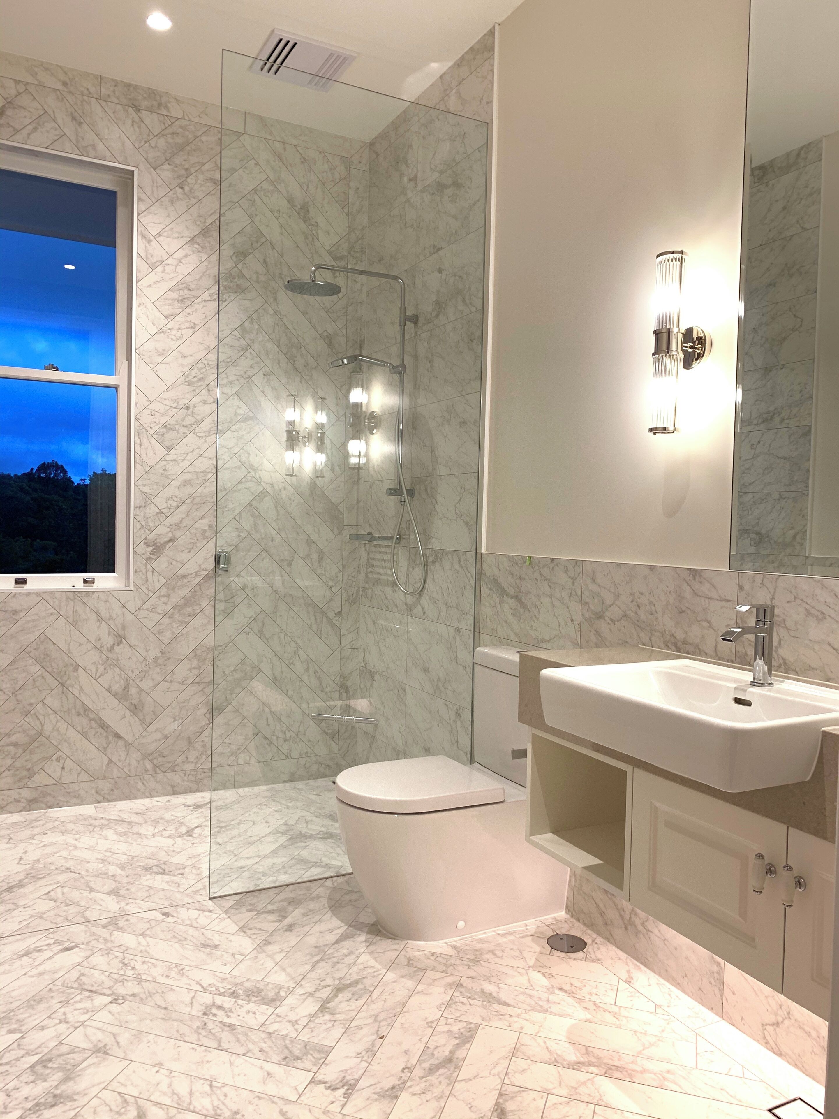A modern bathroom with a glass-enclosed shower, a toilet, and a sink with a large mirror above it.