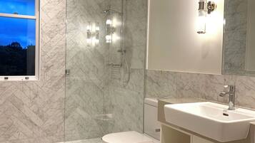A modern bathroom with a glass-enclosed shower, a toilet, and a sink with a large mirror above it.