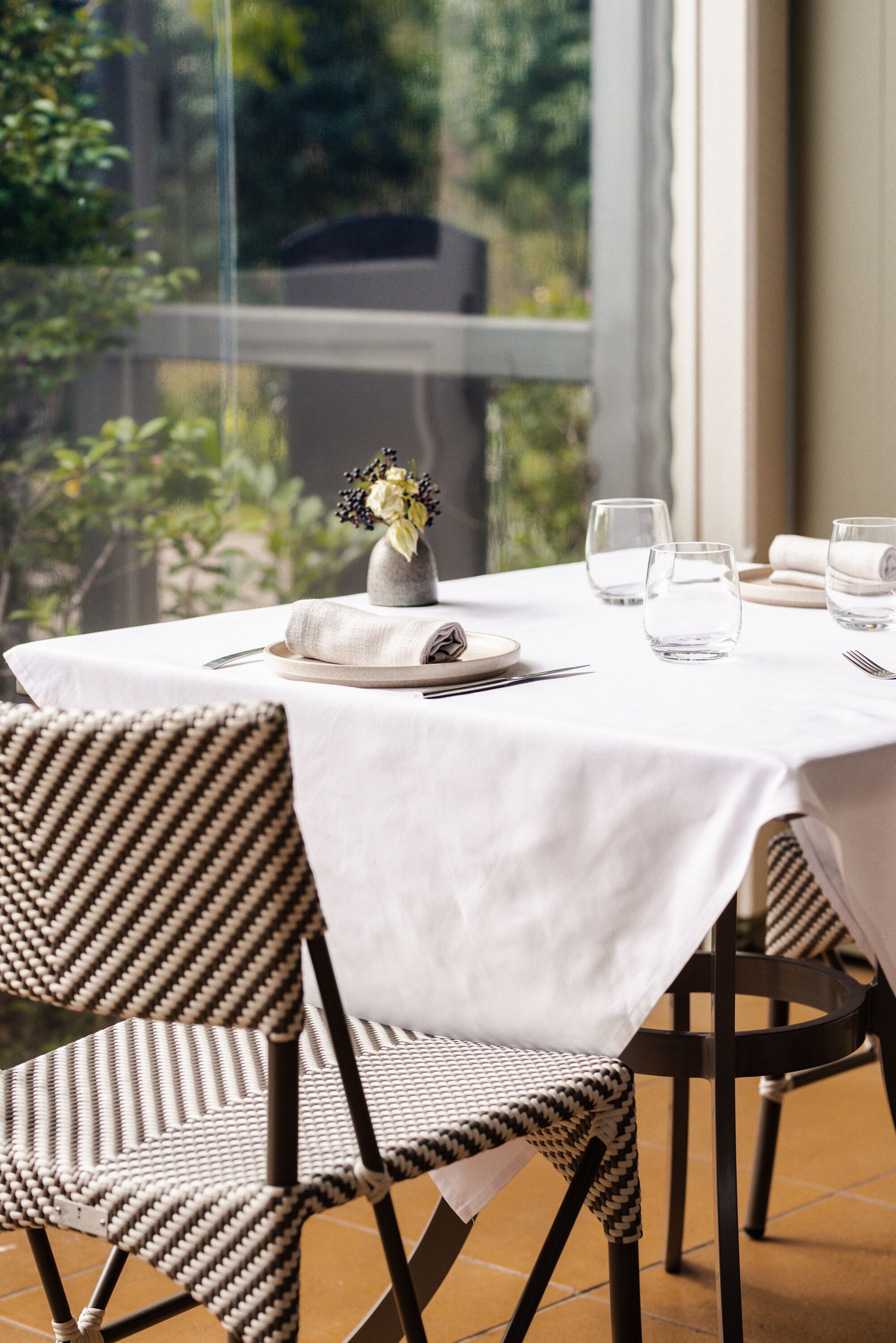 A dining table set with a white tablecloth, two chairs, a vase with flowers, and three glasses.