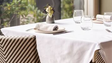 A dining table set with a white tablecloth, two chairs, a vase with flowers, and three glasses.