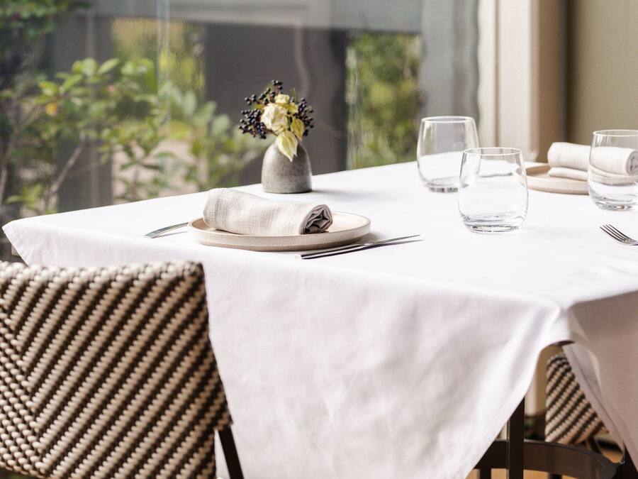 A dining table set with a white tablecloth, two chairs, a vase with flowers, and three glasses.