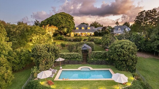 A large house with a swimming pool surrounded by well-maintained gardens and hedges.