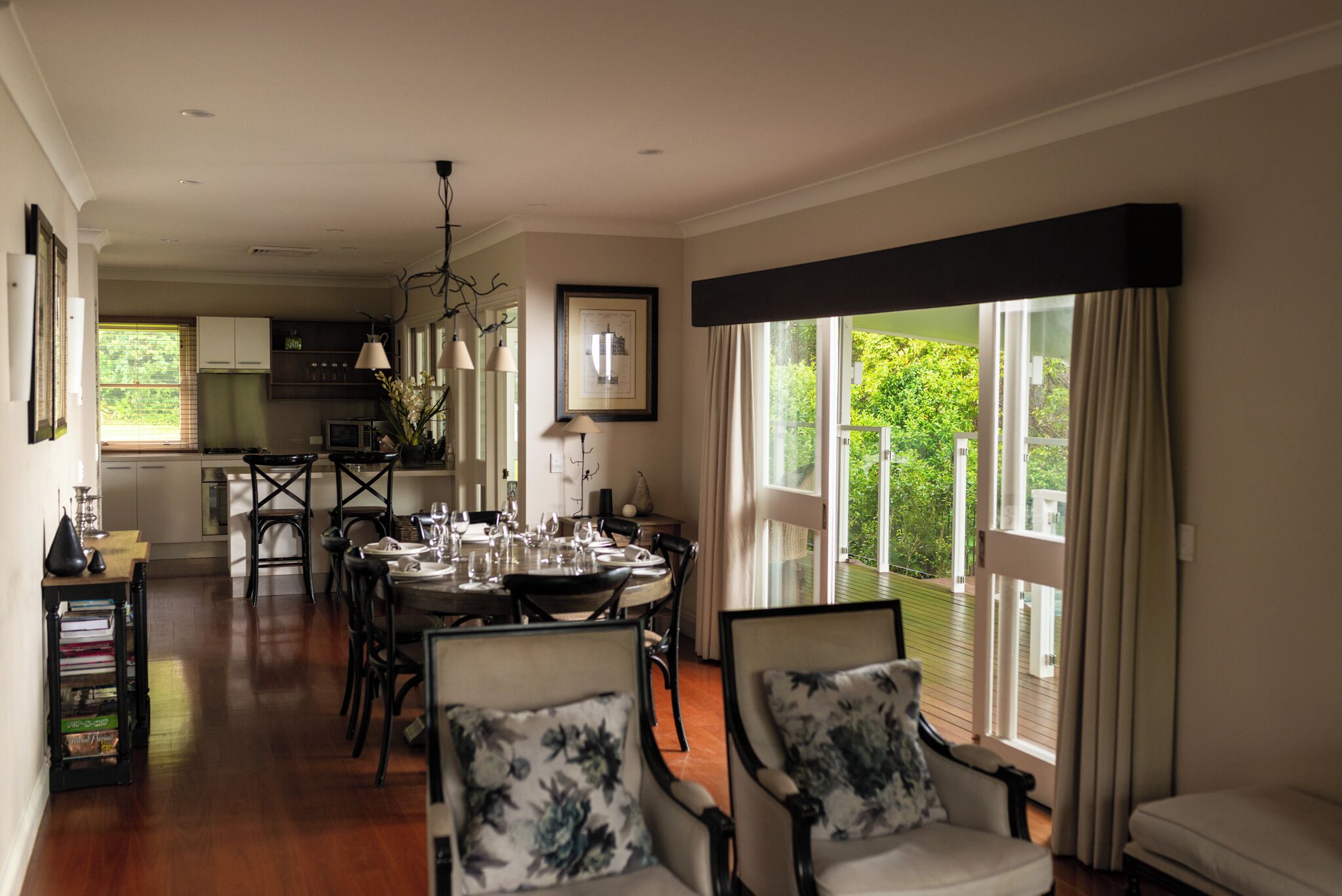 A dining area with a round table set for six, surrounded by chairs with floral cushions. A kitchen is visible in the background with white cabinets and a refrigerator.