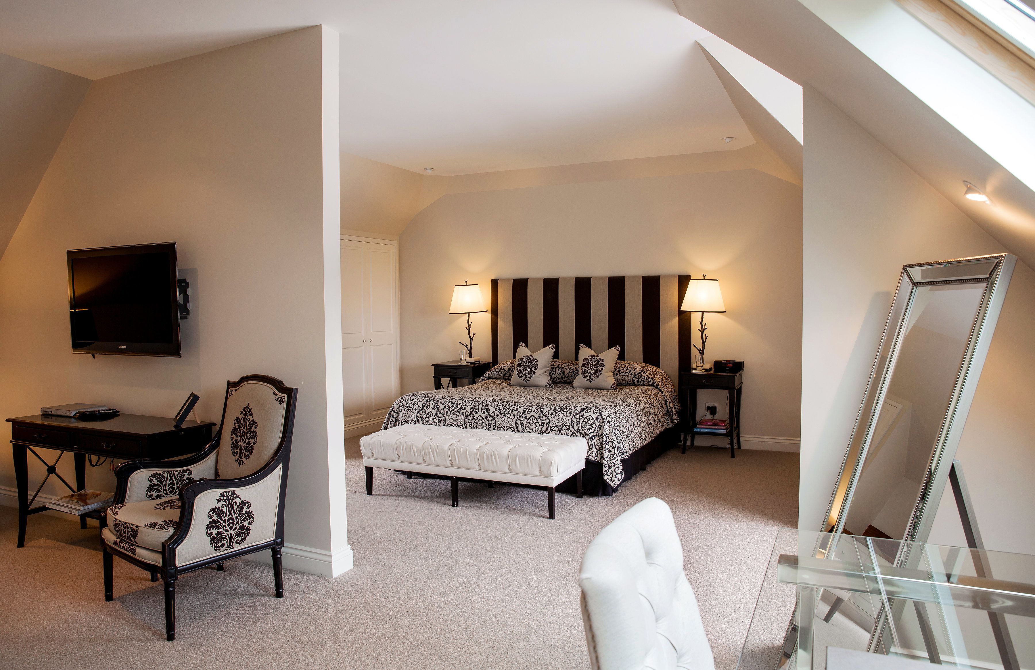 A bedroom with a bed, bedside tables, a desk, a chair, a TV, and a large mirror.