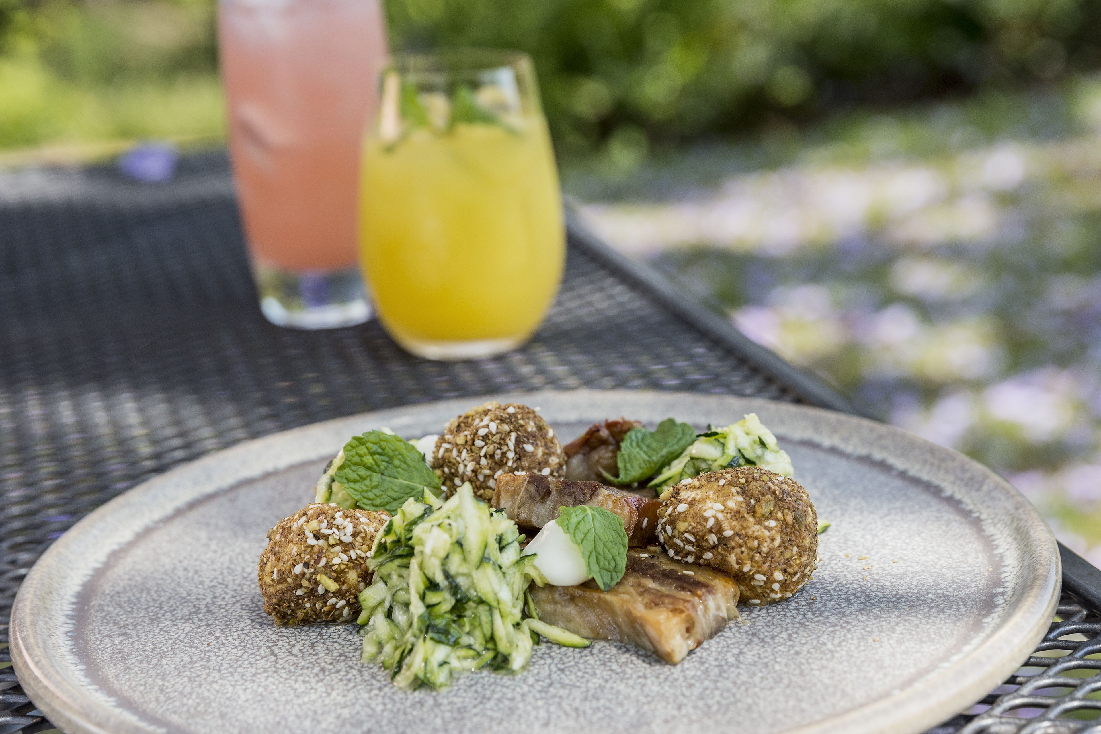 A plate of food with meatballs and a cucumber salad, accompanied by a glass of orange juice on a metal table.