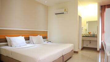 A hotel room with a large bed, a bedside table, an air conditioning unit, a bathroom with a sink and mirror, and a door leading to another room.