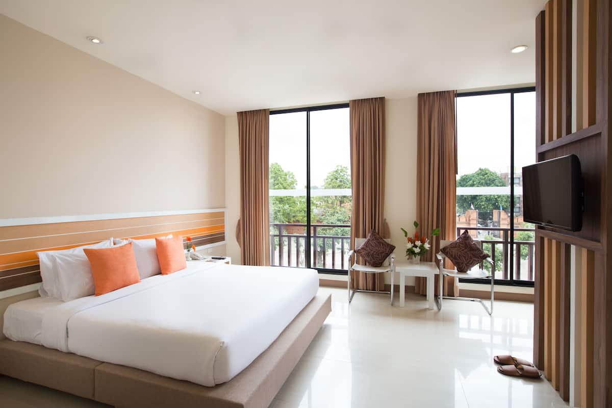 Ein Hotelzimmer mit einem großen Bett, einem Fernseher, einem Balkon mit Tisch und Stühlen sowie Blick auf die Stadt.