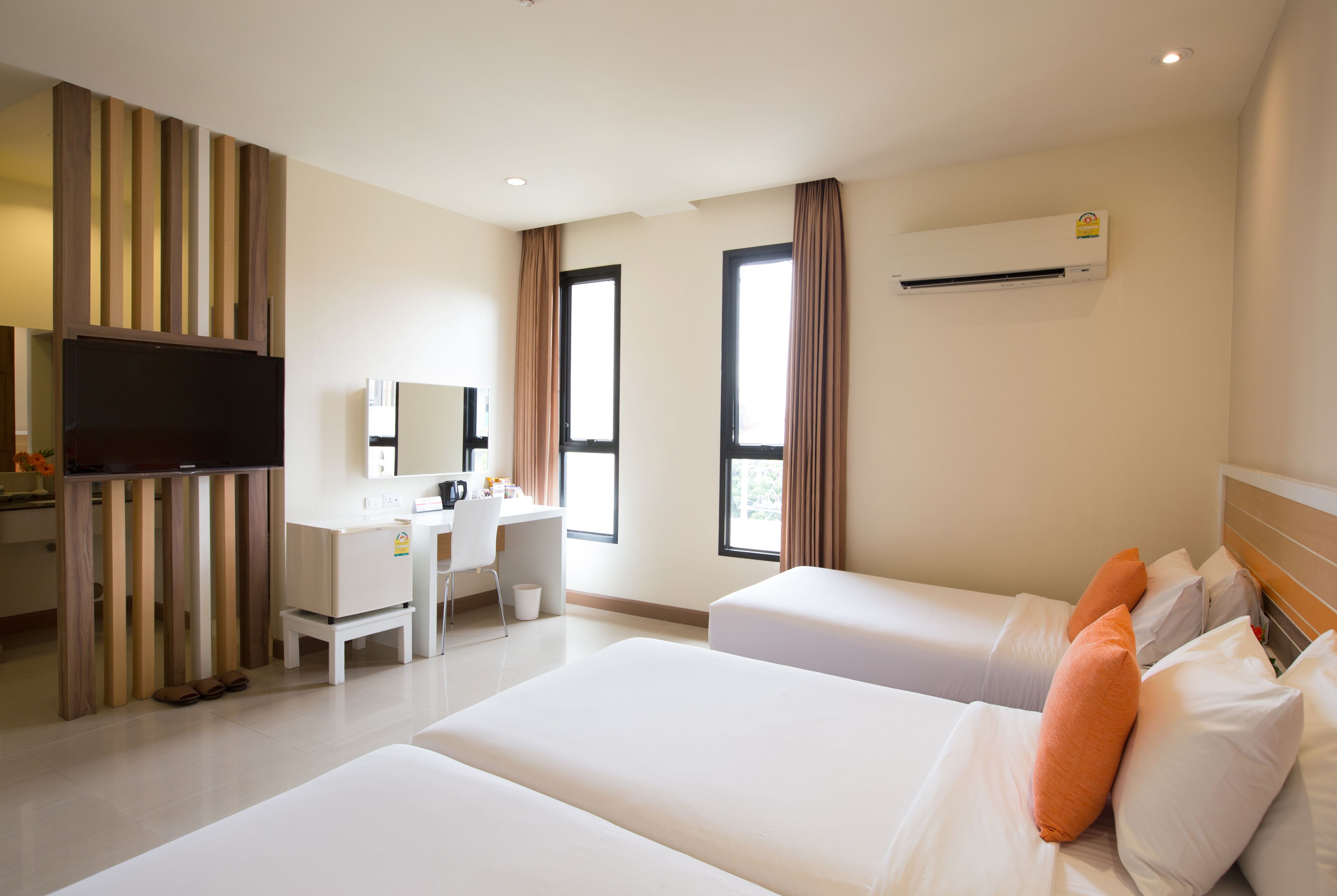 A hotel room with two beds, a desk, a TV, and an air conditioning unit.