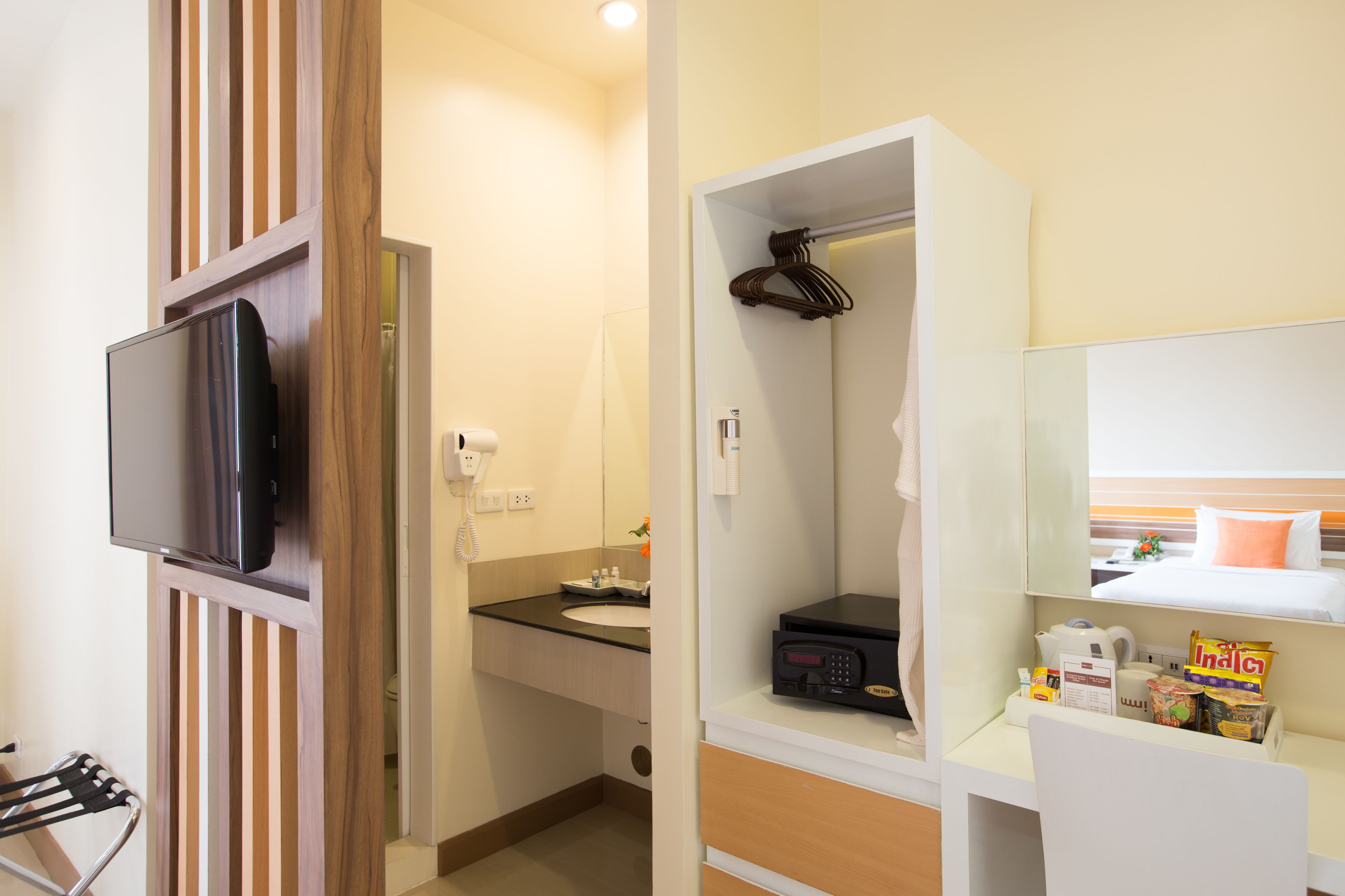 Habitación de hotel pequeña y funcional con televisión de pantalla plana, lavamanos, espejo, armario y un rincón de descanso.