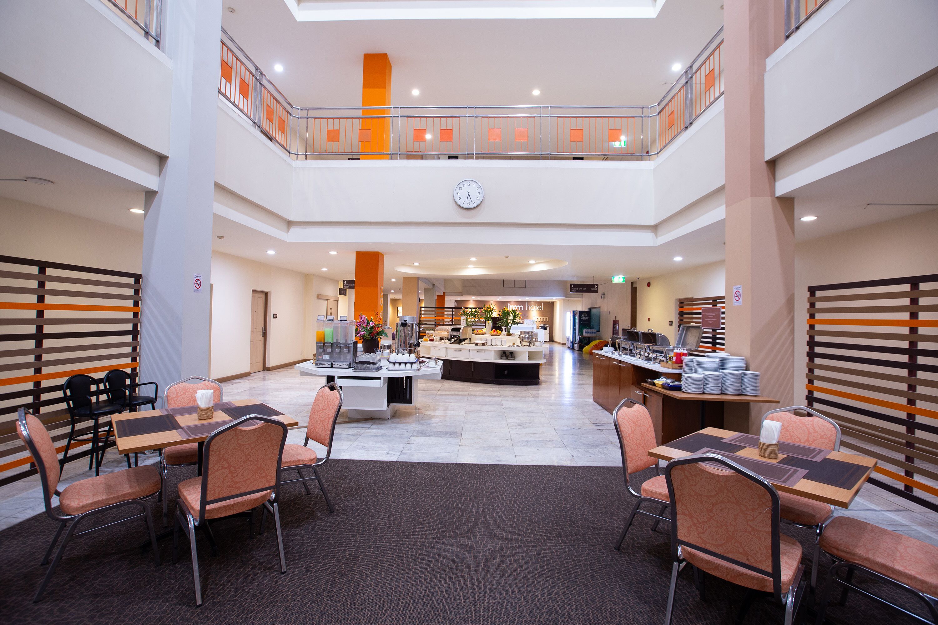 A hotel lobby with a central island, seating areas, and a mezzanine level with a railing.