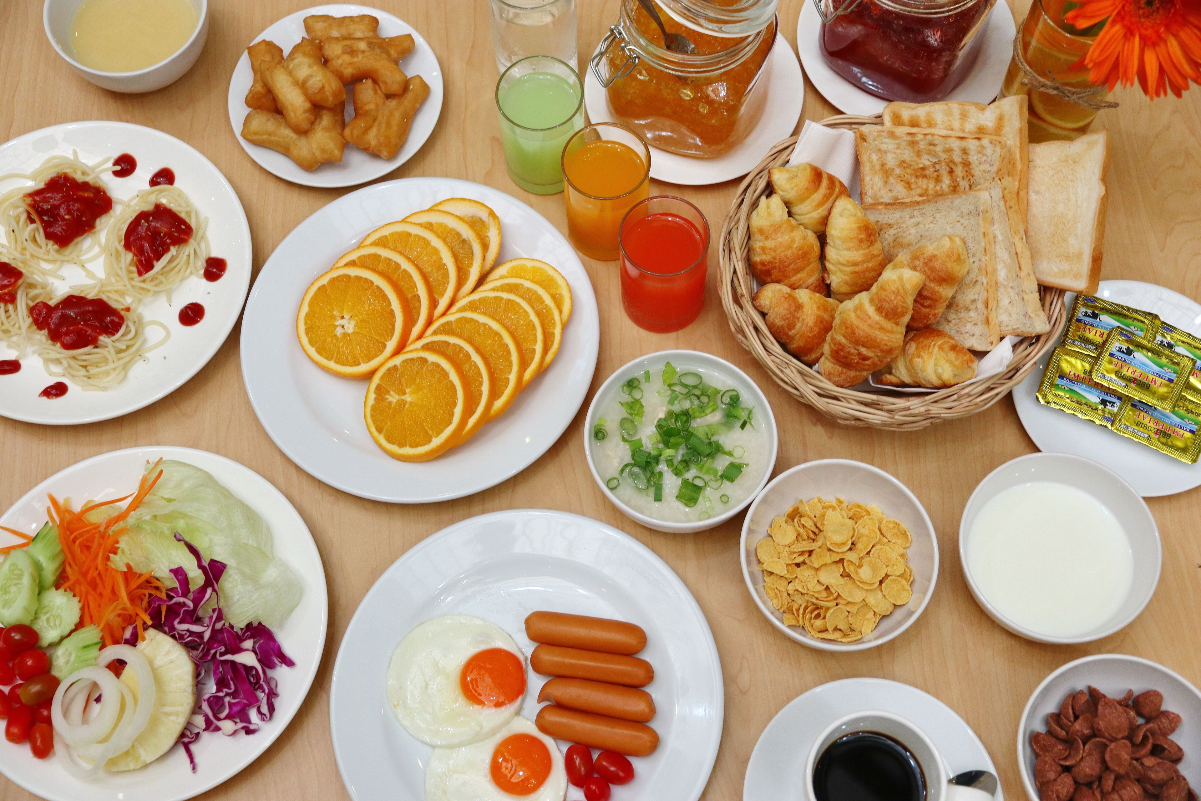 Una mesa con diversos productos para el desayuno, como huevos, salchichas, cruasanes y gajos de naranja.