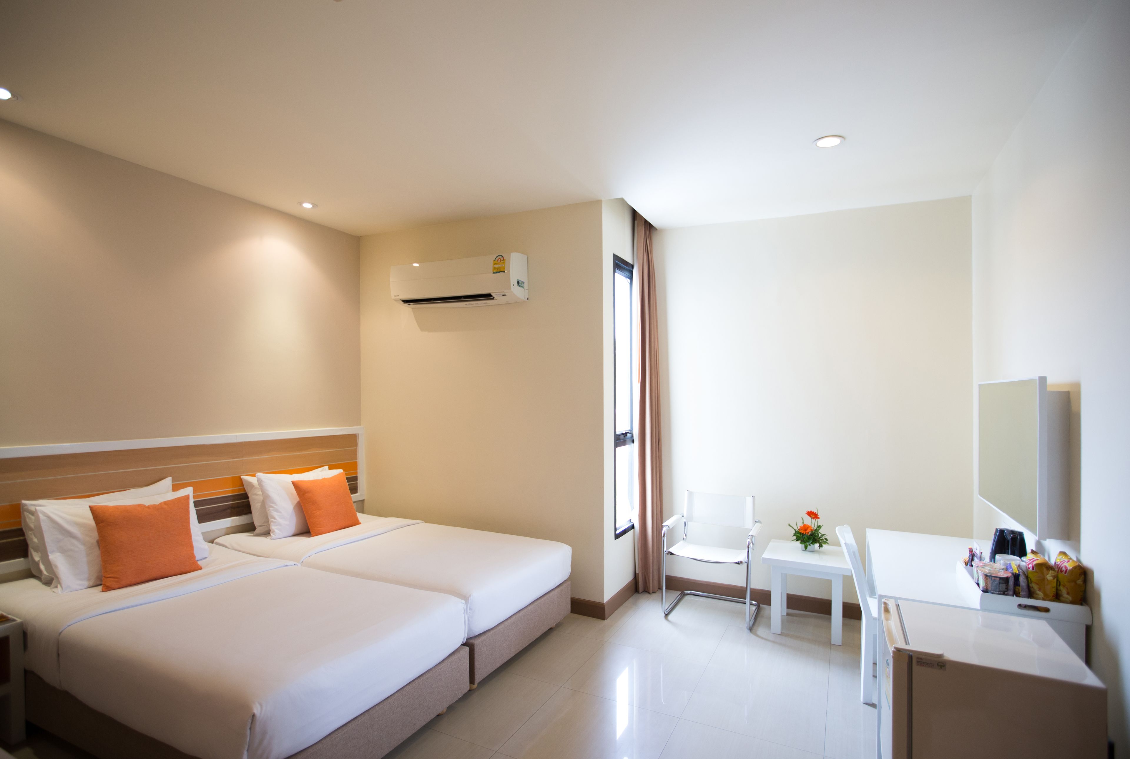 Quarto de hotel com duas camas, uma mesa, uma cadeira e um frigorífico.