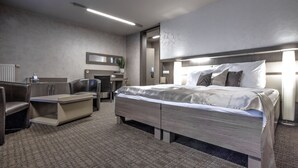 A modern hotel room with a large bed, a desk, a chair, and a small seating area.