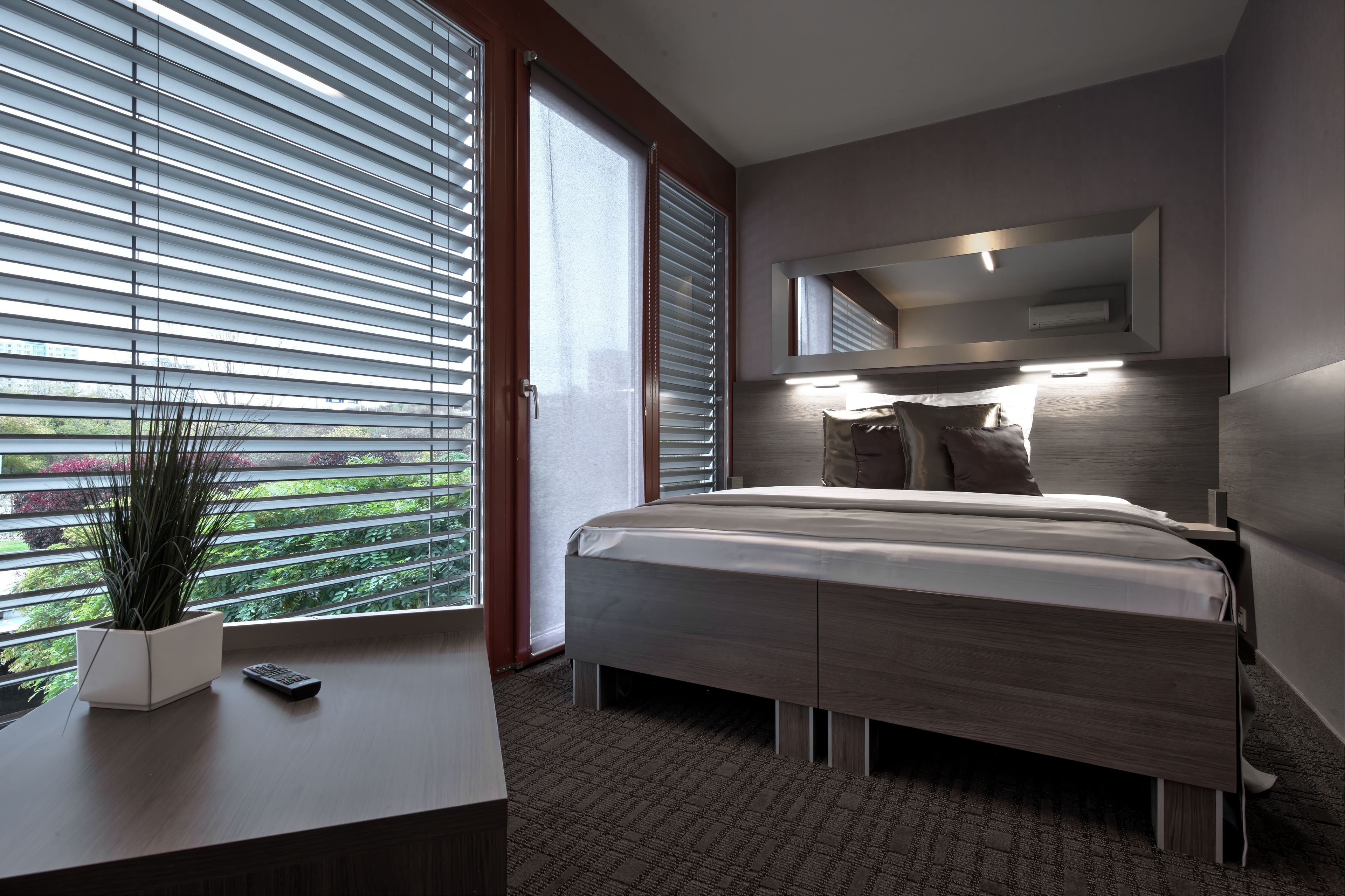 A modern bedroom with a bed, bedside table, and a large window with blinds.