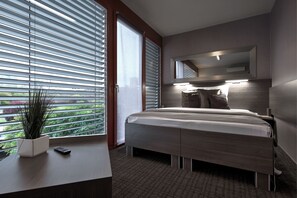 A modern bedroom with a bed, bedside table, and a large window with blinds. - Volcano Spa Hotel (Prague)