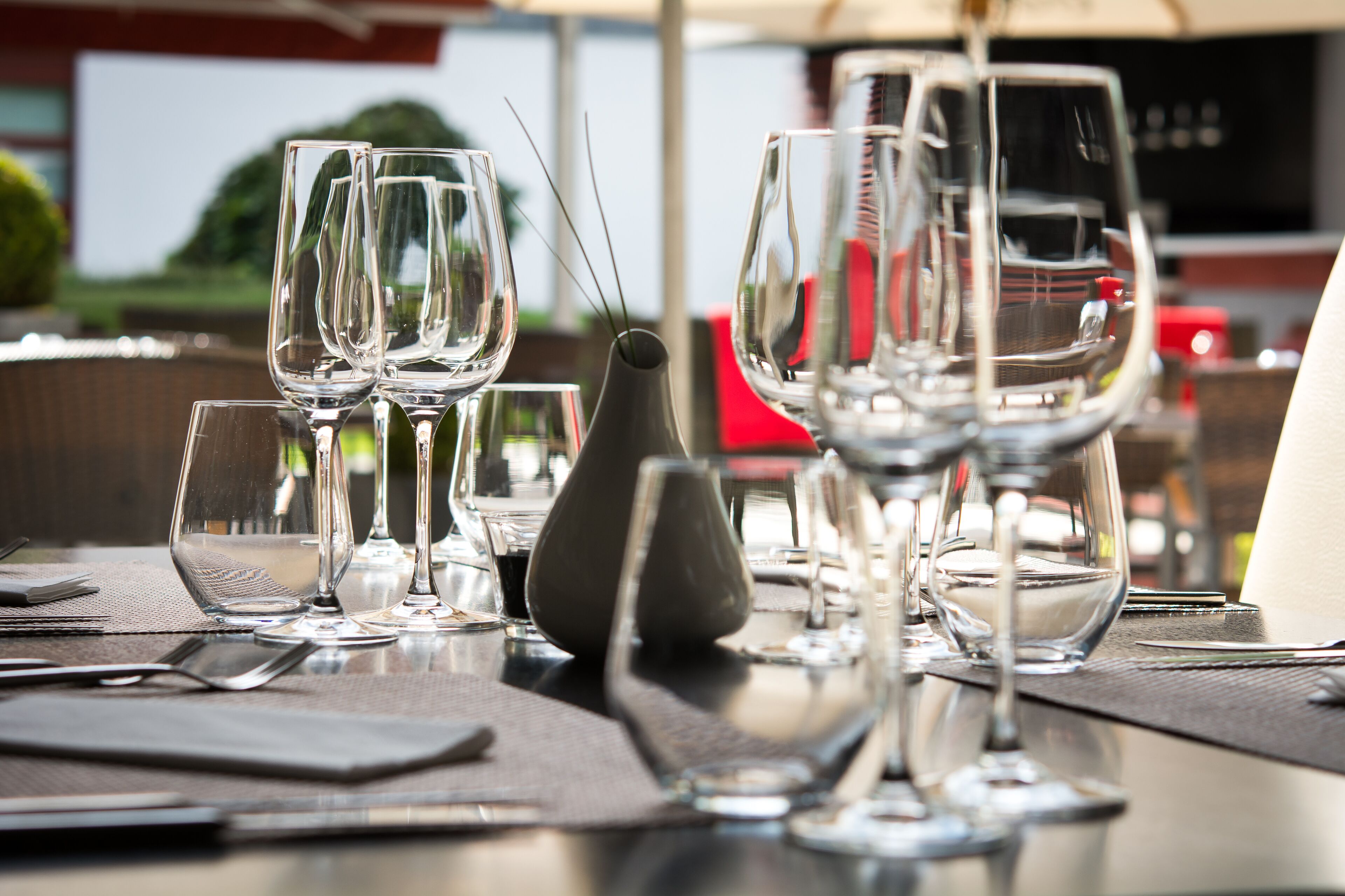 Una mesa de comedor dispuesta con varias copas de vino, un jarrón y cubiertos.
