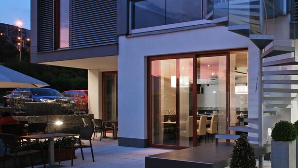 A modern building with a glass facade, a staircase, and a dining area outside.