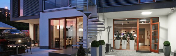 A modern building with a glass facade, a staircase, and a dining area outside. - Volcano Spa Hotel (Prague)