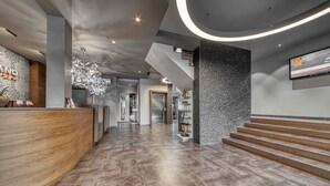 Eine moderne Hotelhalle mit einer Rezeption, einer Treppe und einem großen, an der Wand befestigten Fernseher.