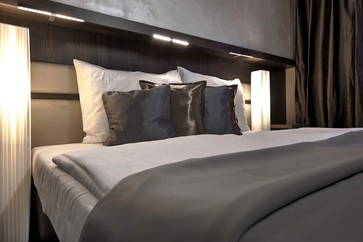 A neatly made bed with a headboard, a bedside lamp, and a window with curtains.
