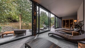 Ein moderner Außenbereich mit Korbmöbeln, großen Glasfenstern und Blick auf einen Garten.
