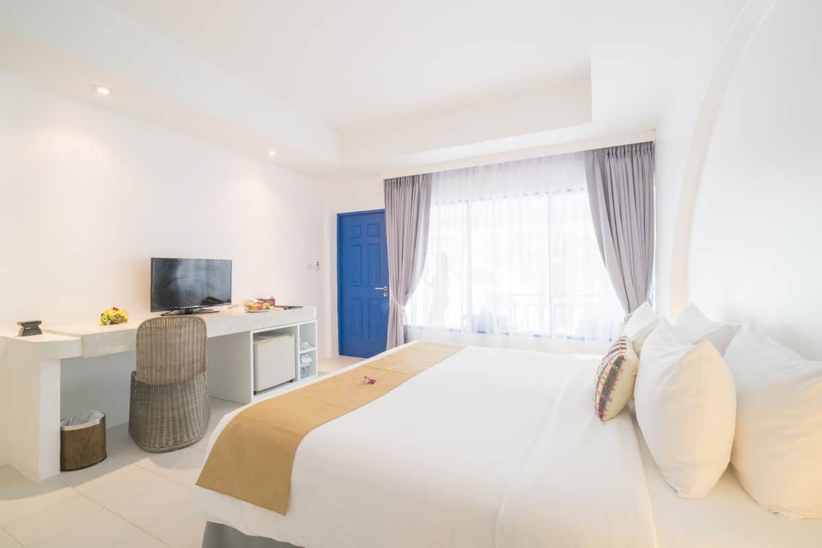 Een hotelkamer met een bed, een bureau met een televisie, een stoel, een prullenbak en een raam met gordijnen.