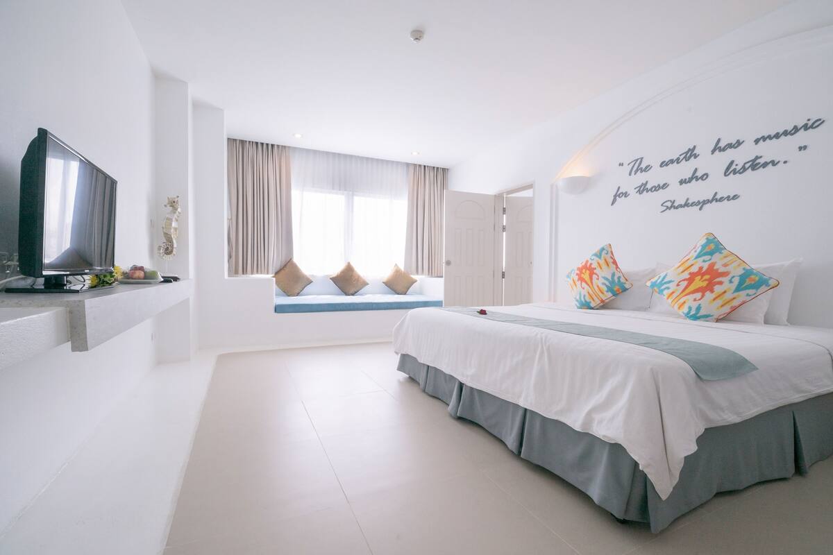 Een moderne hotelkamer met een groot bed, een flatscreen televisie, een raam met gordijnen en een citaat op de muur.