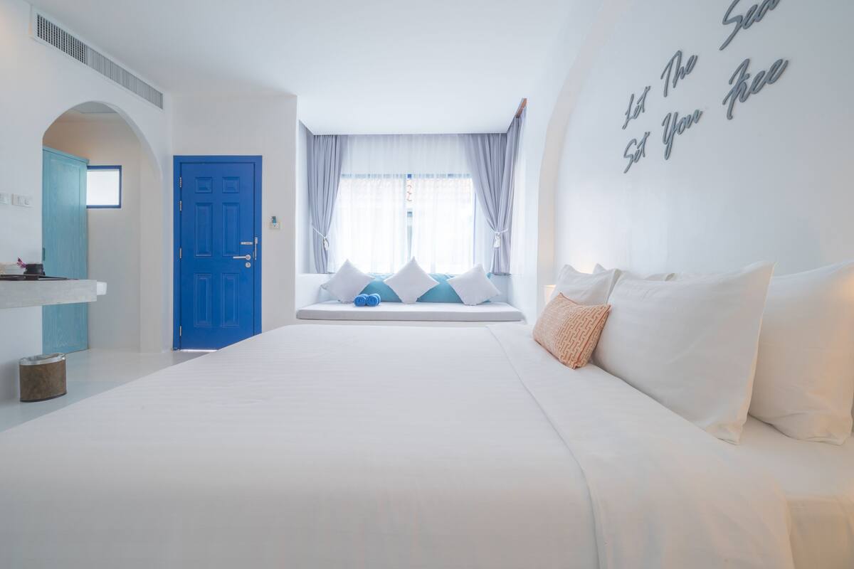 Een slaapkamer met een groot bed, een blauwe deur en een raam met gordijnen.