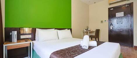 A hotel room with a large bed, a bedside table with a lamp, a desk with a chair, and a door with a sign.