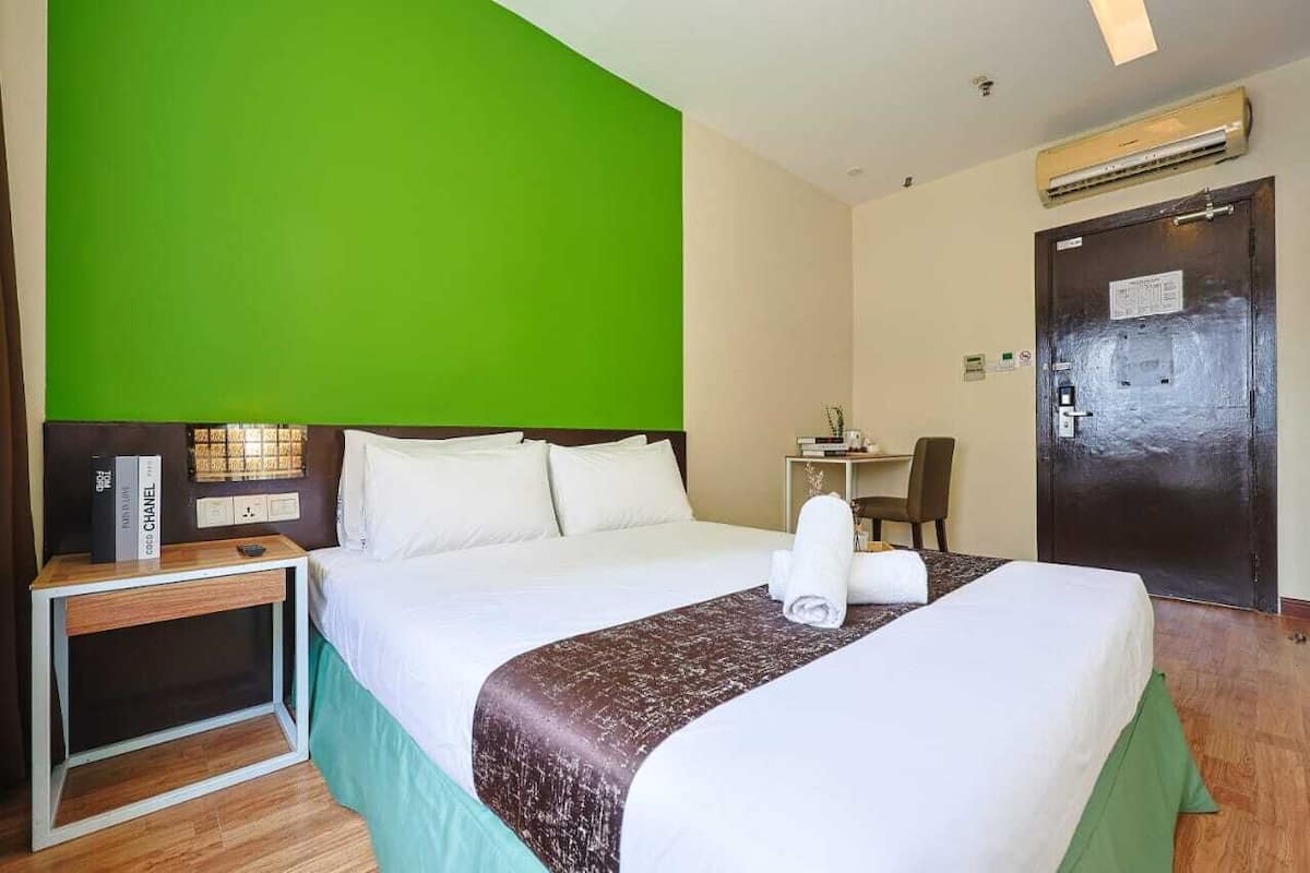 Une chambre d’hôtel avec un grand lit, une table de chevet avec une lampe, un bureau avec une chaise et une porte avec une pancarte.