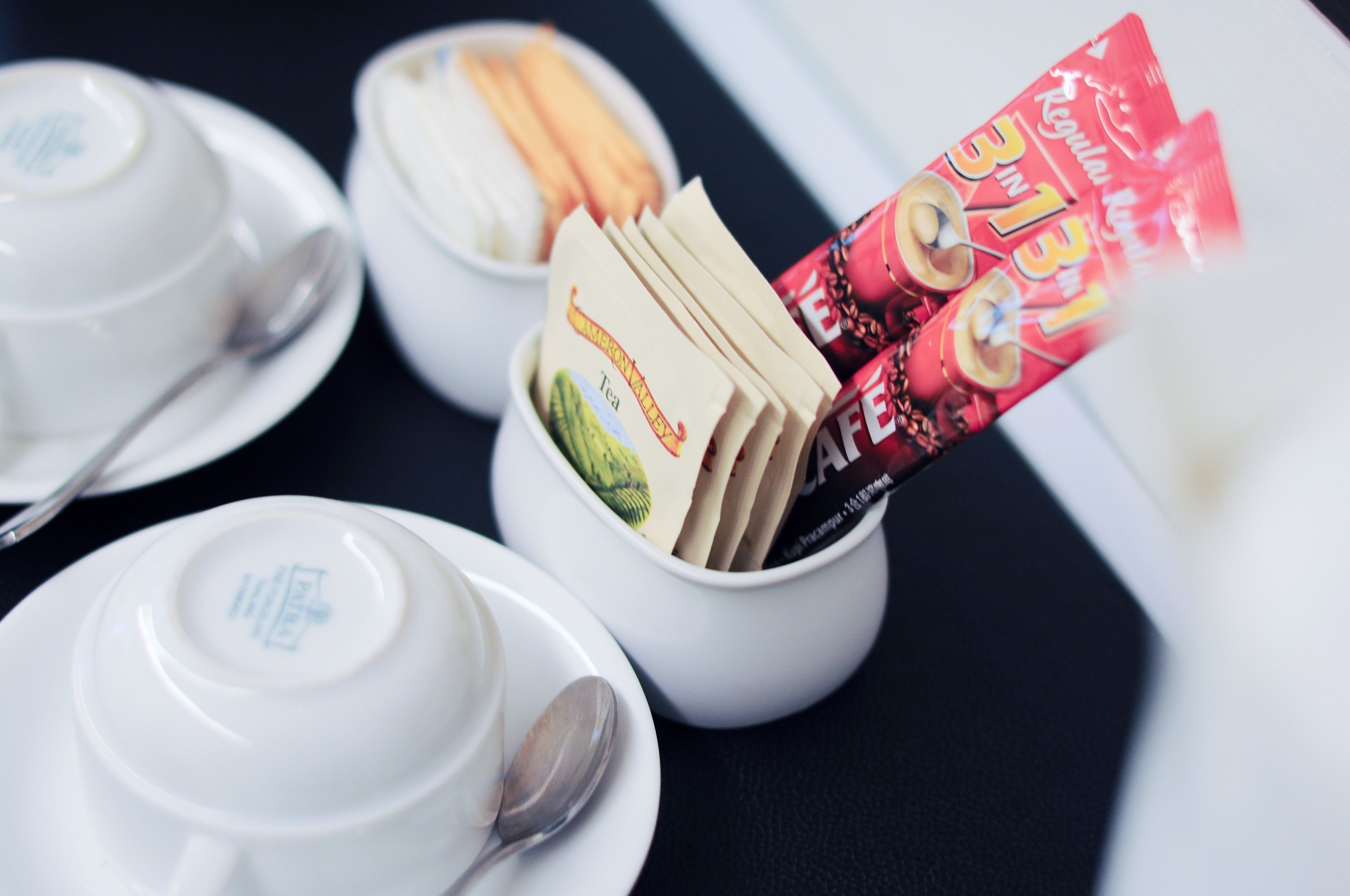 A table with white teacups and saucers, a bowl of tea bags, and a packet of instant coffee.