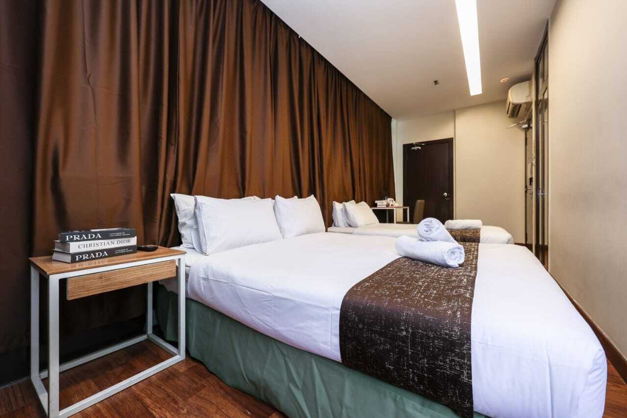A hotel room with a large bed, a bedside table with books, and a bathroom visible through an open door.