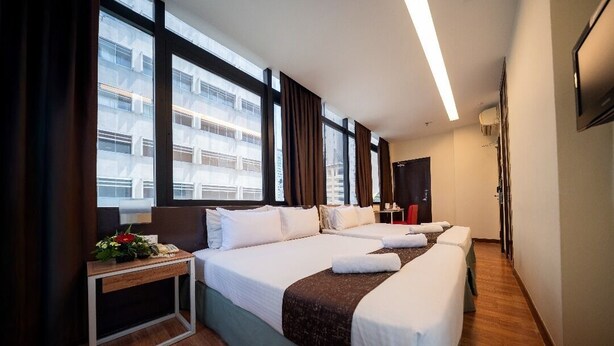 Une chambre d’hôtel avec deux lits, un bureau, une chaise, une petite table avec une plante et une vue sur les bâtiments à travers de grandes fenêtres.