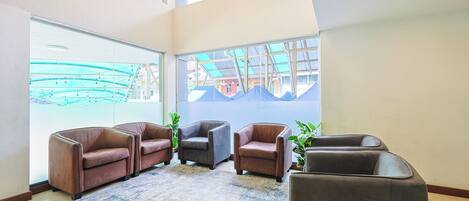 A spacious lobby with leather armchairs, a patterned rug, and large windows offering views of the outside.