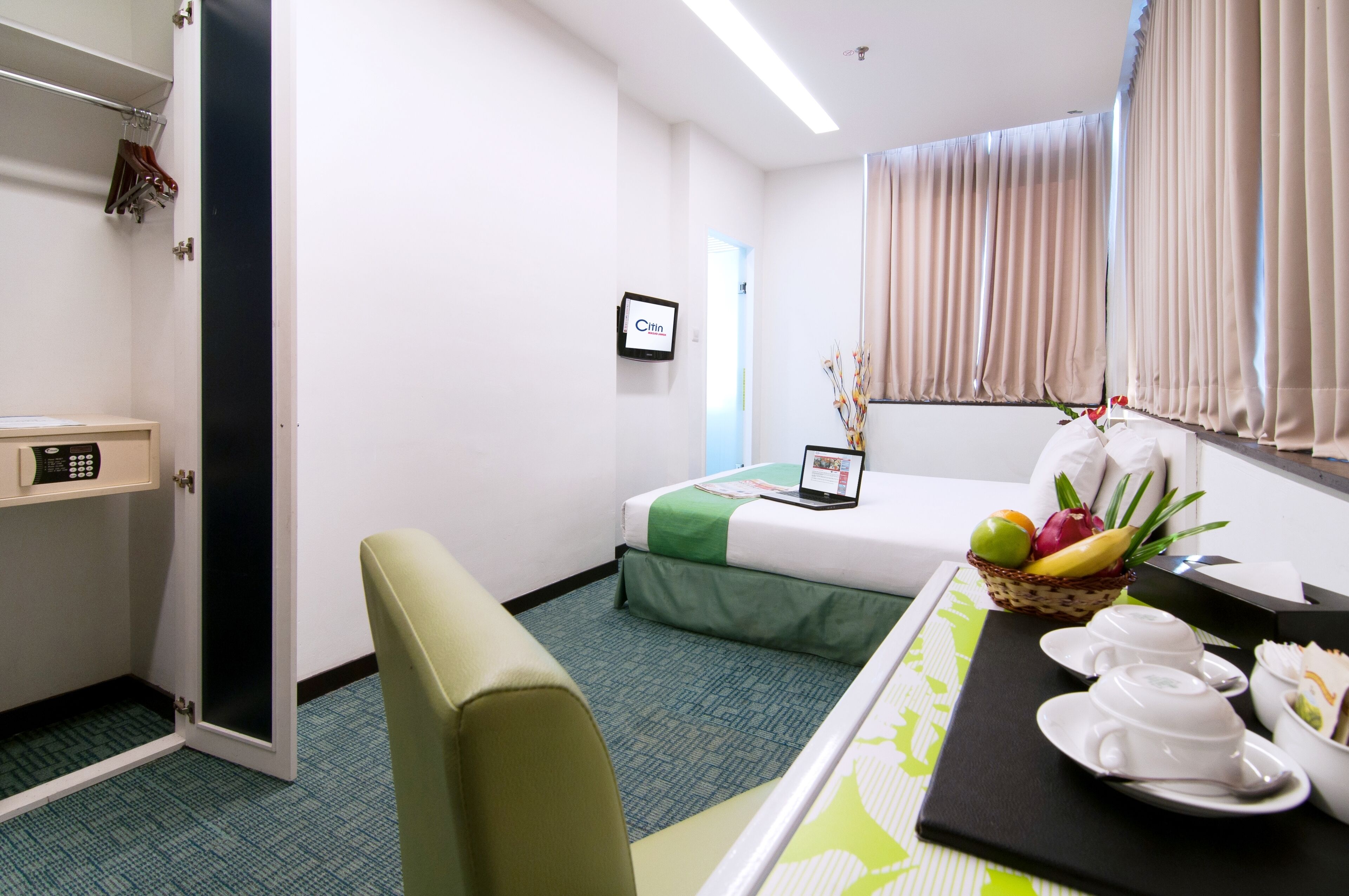 Une chambre d’hôtel avec un lit, un bureau avec un ordinateur portable, un panier de fruits et un plateau de petit-déjeuner.