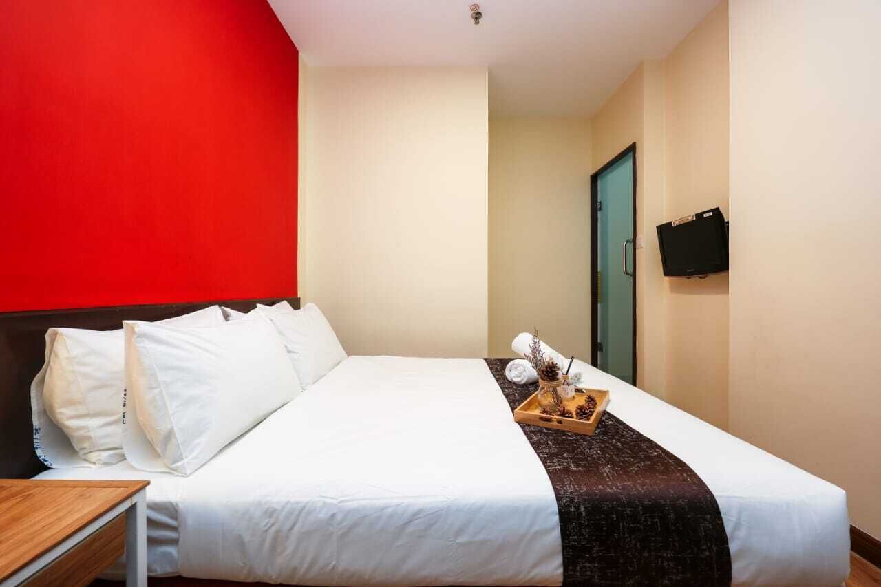 Una habitació d'hotel amb un llit, una tauleta de nit de fusta, una safata amb articles de tocador, una televisió penjada a la paret i una porta que condueix a una altra habitació.