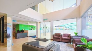 Un hall d’entrée moderne doté d’un comptoir de réception, d’un espace salon et de grandes fenêtres offrant une vue sur l’extérieur.