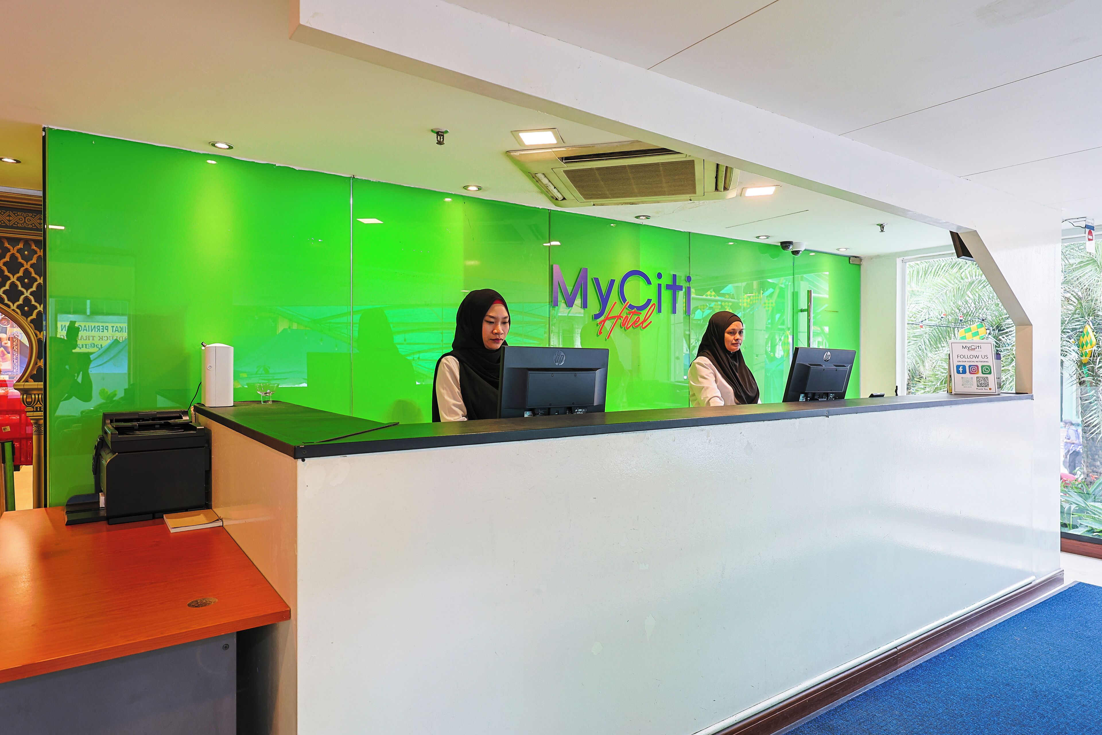 A reception desk with a green backdrop and two receptionists.