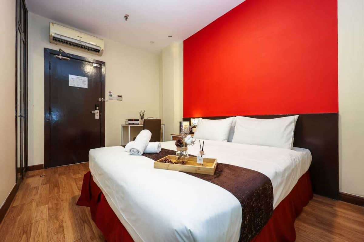 Une chambre d’hôtel avec un grand lit, un mur d’accent rouge, un plancher en bois et une petite table avec un plateau.
