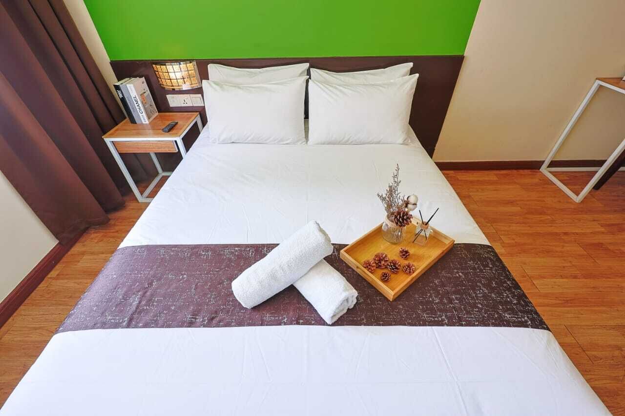 Ein ordentlich gemachtes Bett mit weißen Leinentüchern, ein Holztablett mit Kiefernzapfen und ein zusammengerolltes Handtuch auf einem braunen Bettvorleger.