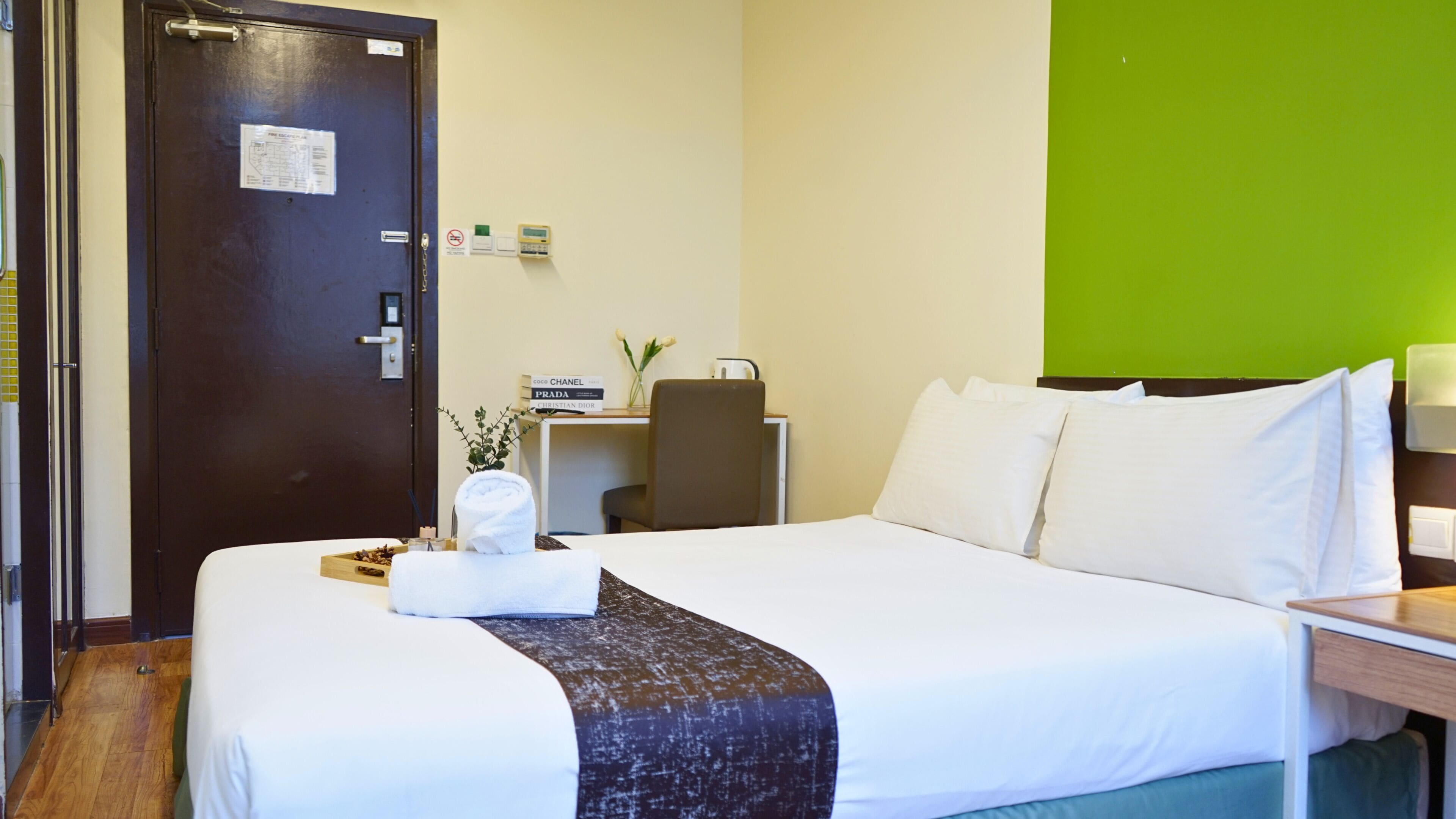 A hotel room with a bed, a desk, a chair, a door, and a green wall.