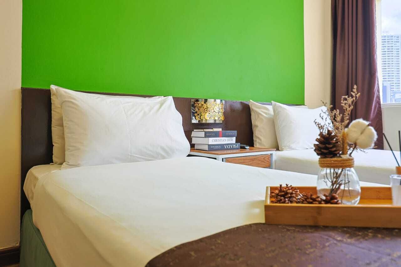 A hotel room with a large bed, a nightstand with books, a vase with pinecones, and a window with curtains.