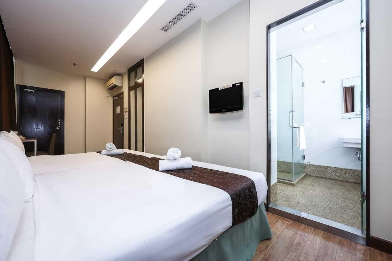 A hotel room with a large bed, a desk, a TV, and a glass door leading to a bathroom.
