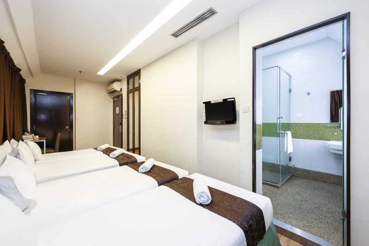Une chambre d’hôtel avec deux lits, une télévision et une douche séparée par des parois en verre.