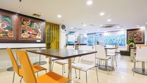 L’intérieur d’un restaurant présente une salle à manger avec une grande table et des chaises, une horloge au mur et des tableaux représentant des plats, accrochés aux murs.