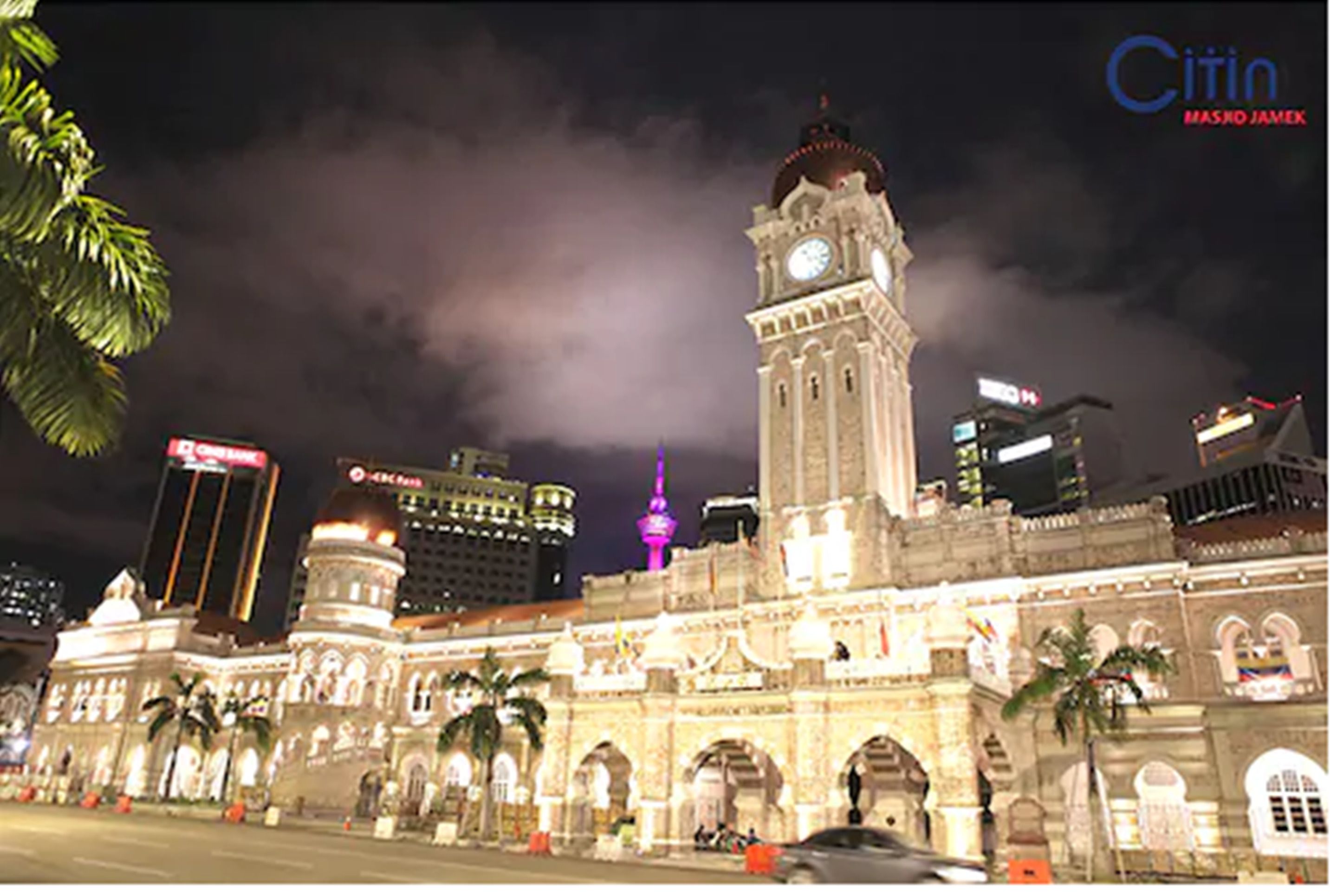 Un edificio histórico con una torre del reloj, palmeras y edificios modernos al fondo.